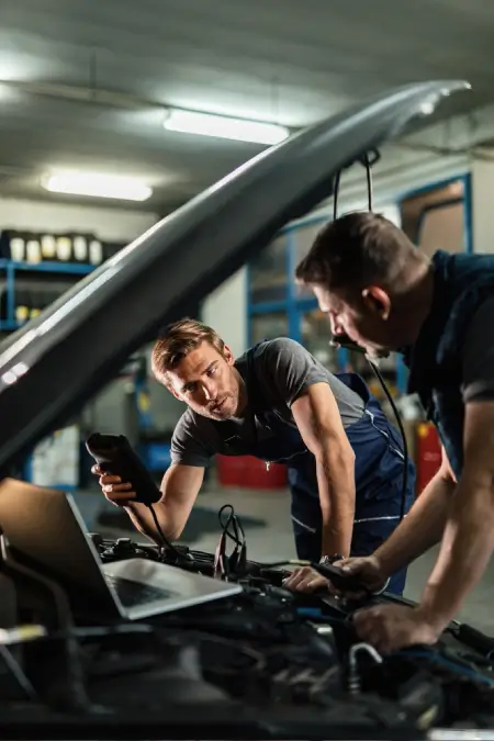 Technician working on a vehicle with the bonnet open in the workshop